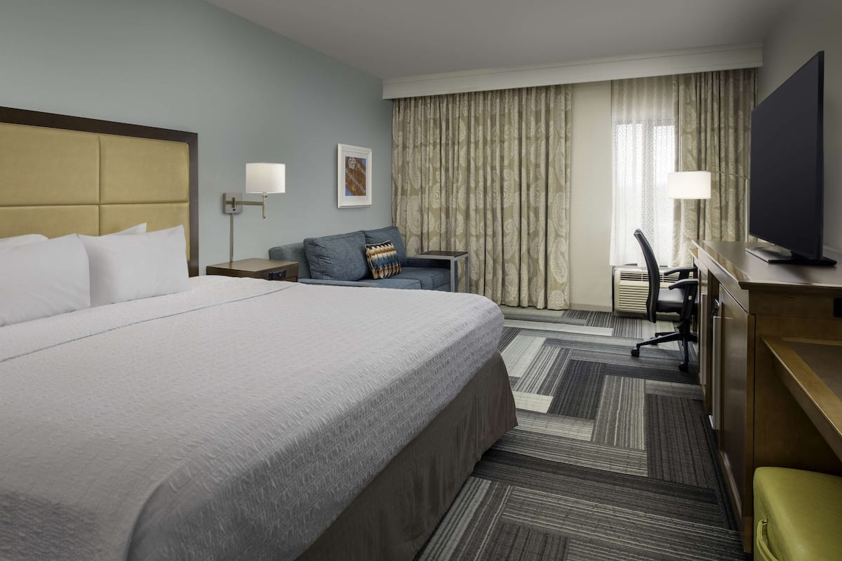 A hotel room with a large bed, a desk with a chair, a television, and a window with curtains.