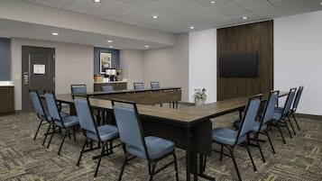 A conference room with a long table, blue chairs, a wooden cabinet, a flat-screen TV, and a patterned carpet.