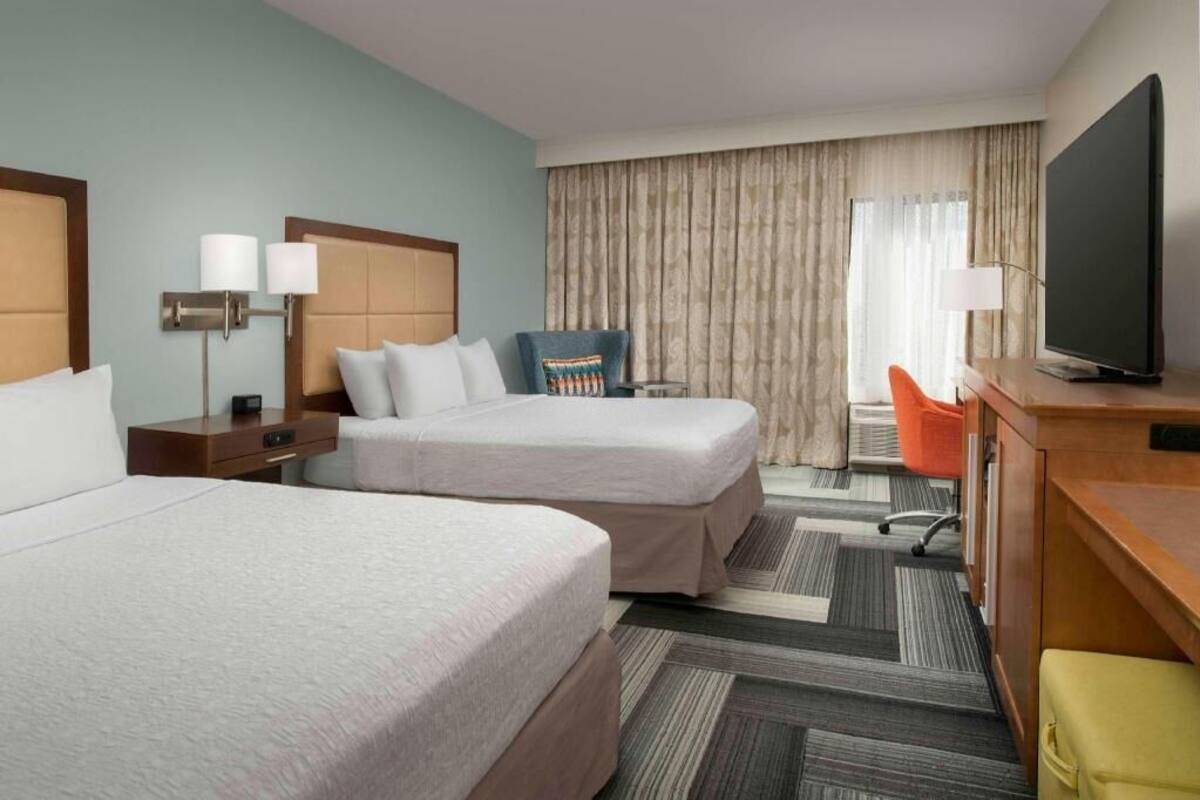 A hotel room with two beds, a desk, a television, and a chair.