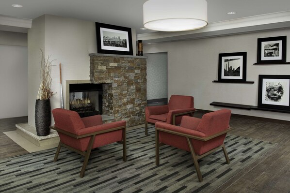 A modern living room with a stone fireplace, red armchairs, a large vase, and framed pictures on the wall.
