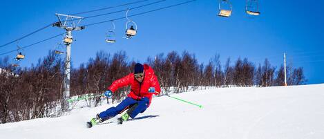 A person skiing down a snowy slope with ski lifts in the background.