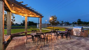 Un patio al aire libre con una pérgola, mobiliario y una parrilla.