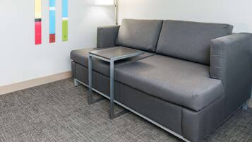 A gray sofa with a small table in front, a carpeted floor, and a wall with colorful vertical elements.
