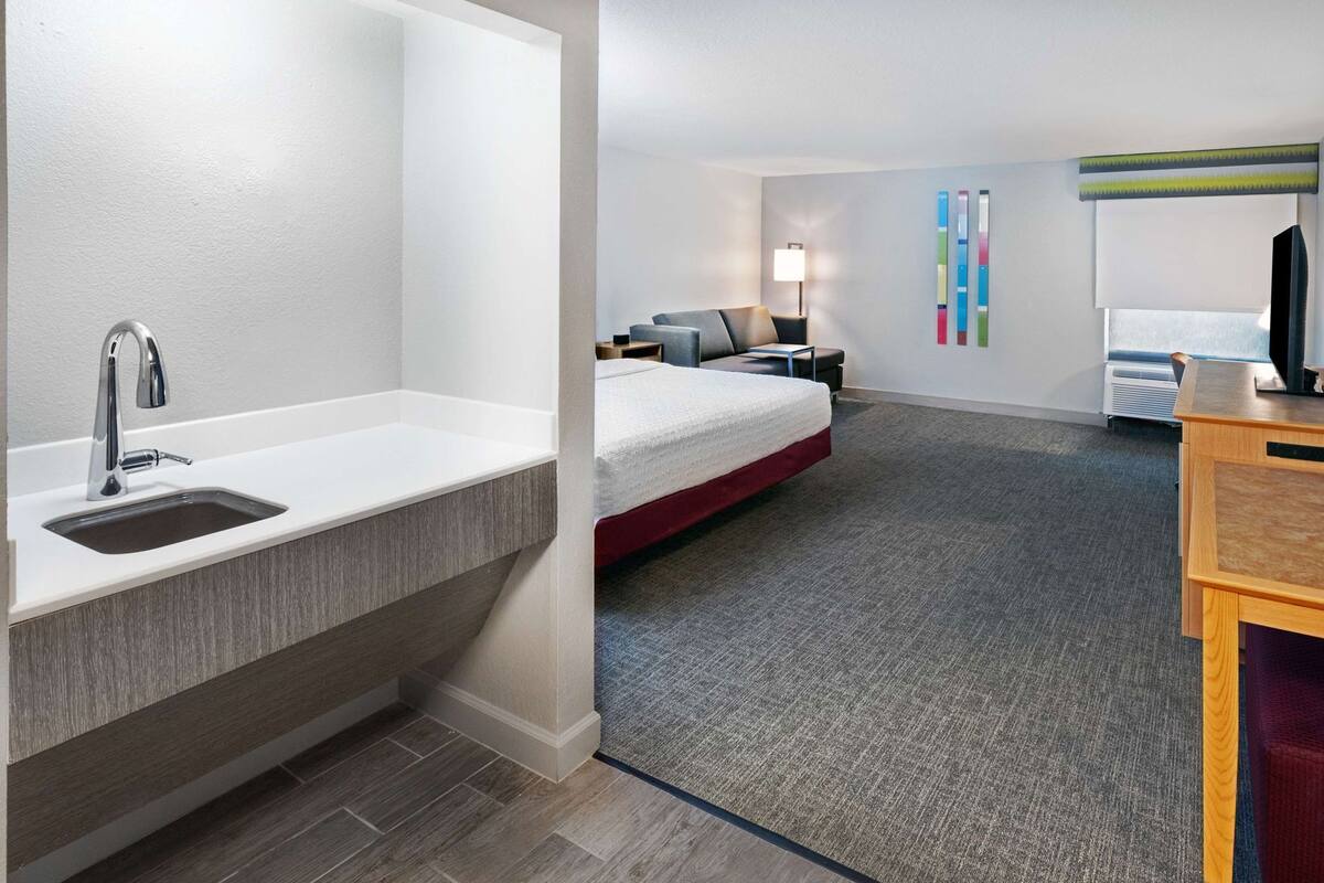 Een hotelkamer met een moderne badkamer, een bed, een bureau en een nachtkastje.