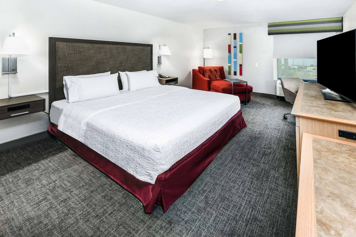 Een hotelkamer met een groot bed, een bureau, een televisie en een rode stoel.