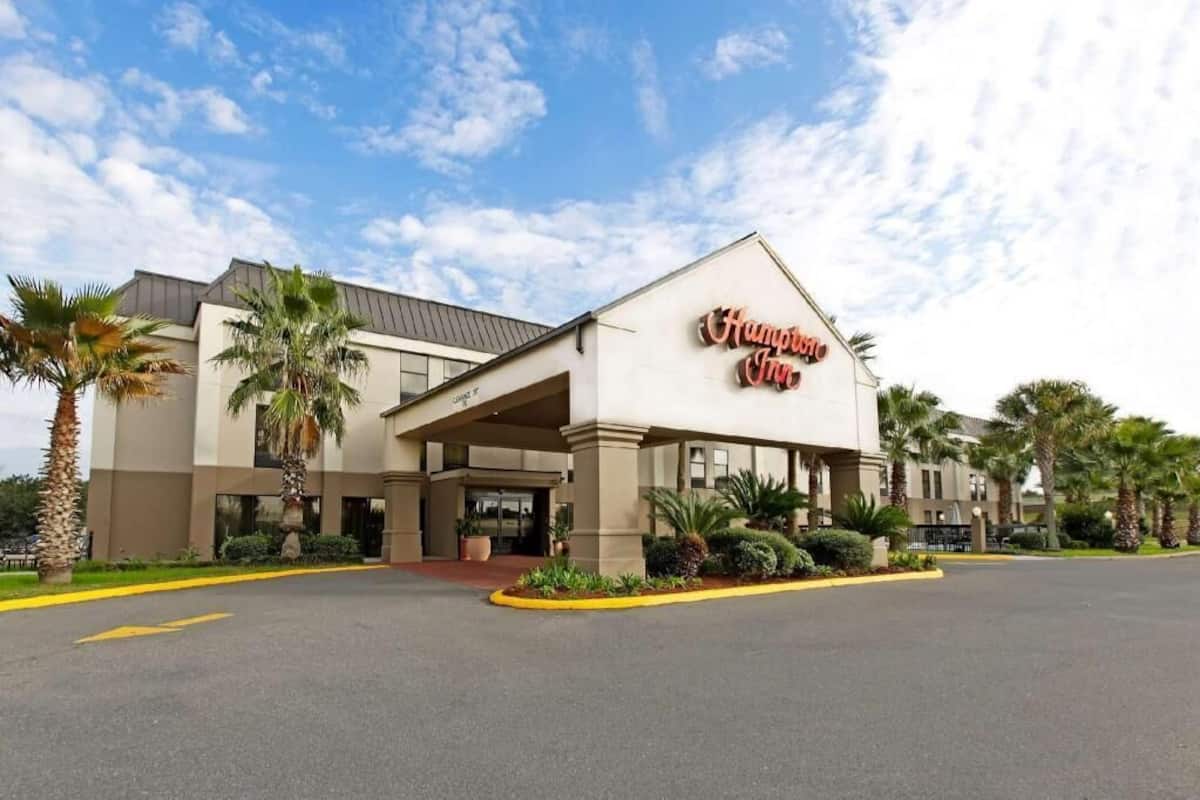 Een hotel met een opvallend 'Hampton Inn' bord, een overdekte ingang en palmbomen.