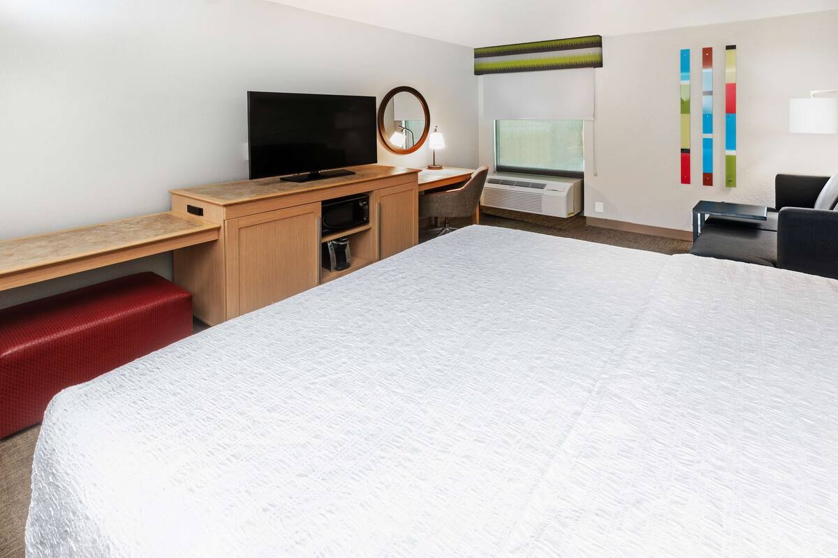 Een hotelkamer met een groot bed, een bureau met televisie, een spiegel, een stoel en een raam met airconditioning.