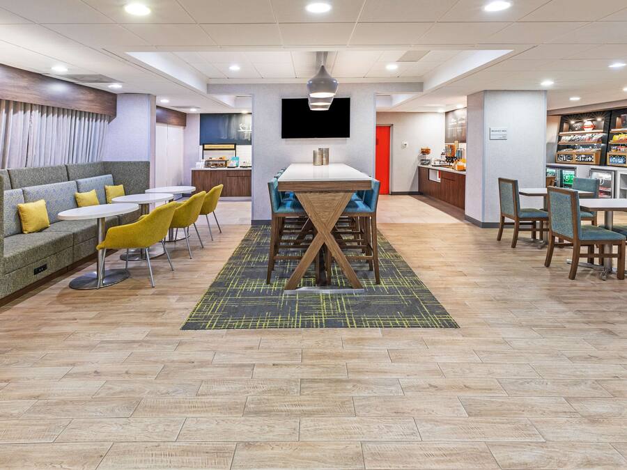 A modern hotel lobby with a seating area, a central table, and a food counter.