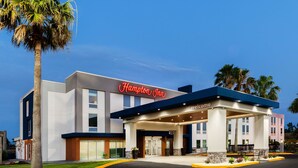 Un hotel Hampton Inn con fachada moderna, una entrada bien iluminada y un área ajardinada con palmeras.