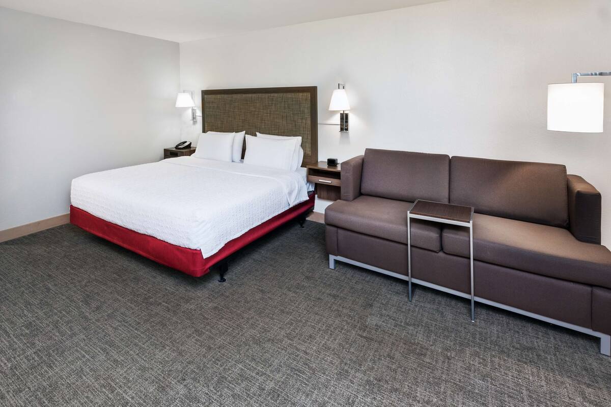 Een hotelkamer met een bed, een bruine bank, een klein tafeltje en twee bedlampjes.