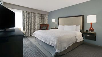 A hotel room with a bed, a television, a chair, a nightstand with a lamp, and a window with curtains.