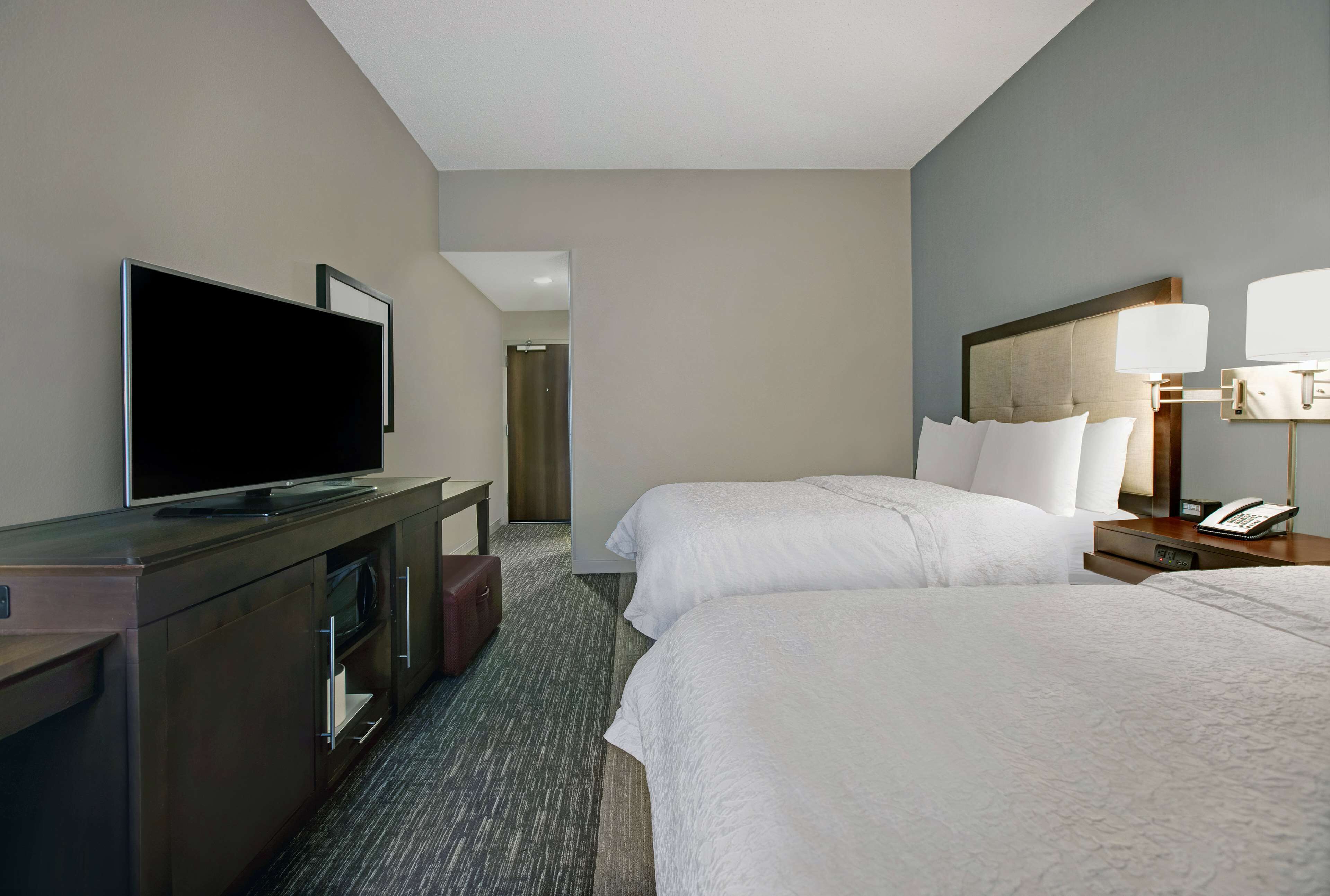 Habitación de hotel con dos camas, un televisor sobre un aparador, un escritorio con lámpara y un teléfono.