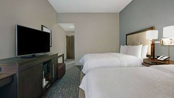 Habitación de hotel con dos camas, un televisor sobre un aparador, un escritorio con lámpara y un teléfono.