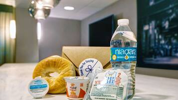 A breakfast tray with a bagel, cream cheese spread, yogurt, eggs, and a bottle of water.