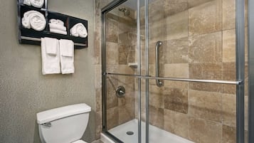 A bathroom with a glass-enclosed shower, a toilet, and a shelf with neatly folded towels.