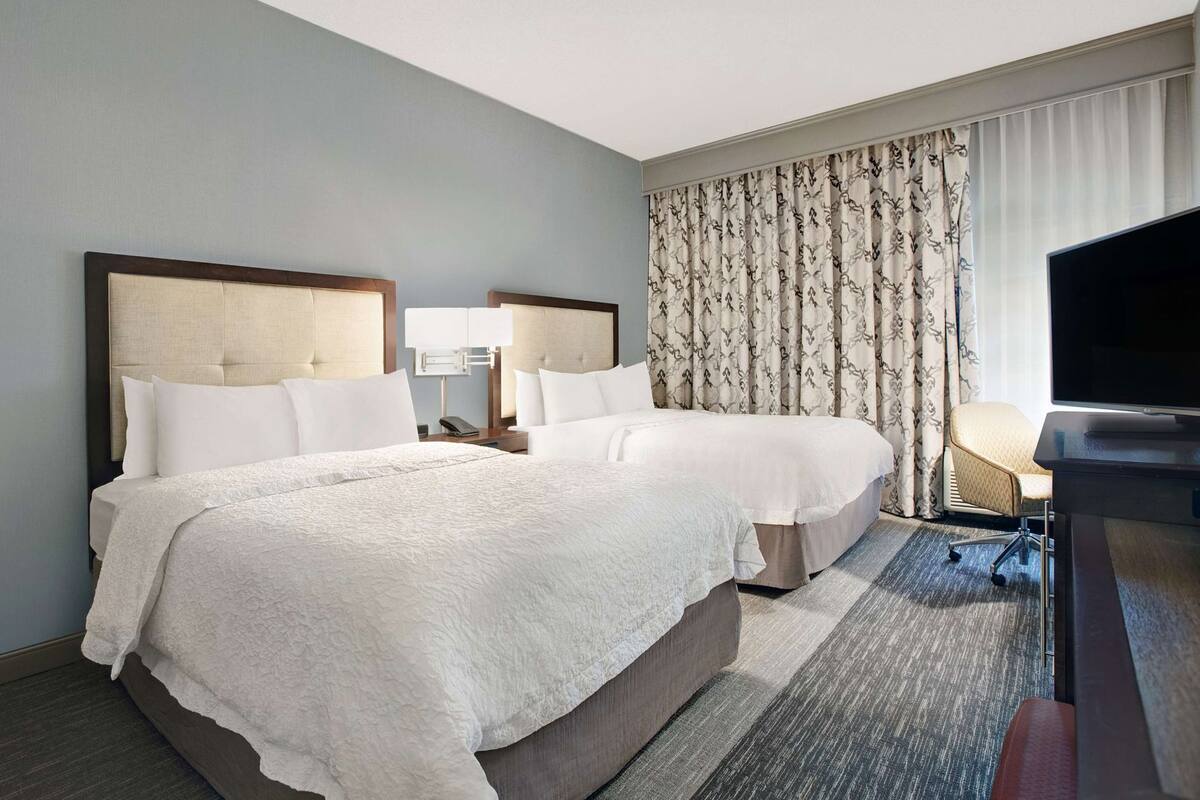 Une chambre d’hôtel avec deux lits, un bureau avec une télévision, une lampe et un rideau à motifs.