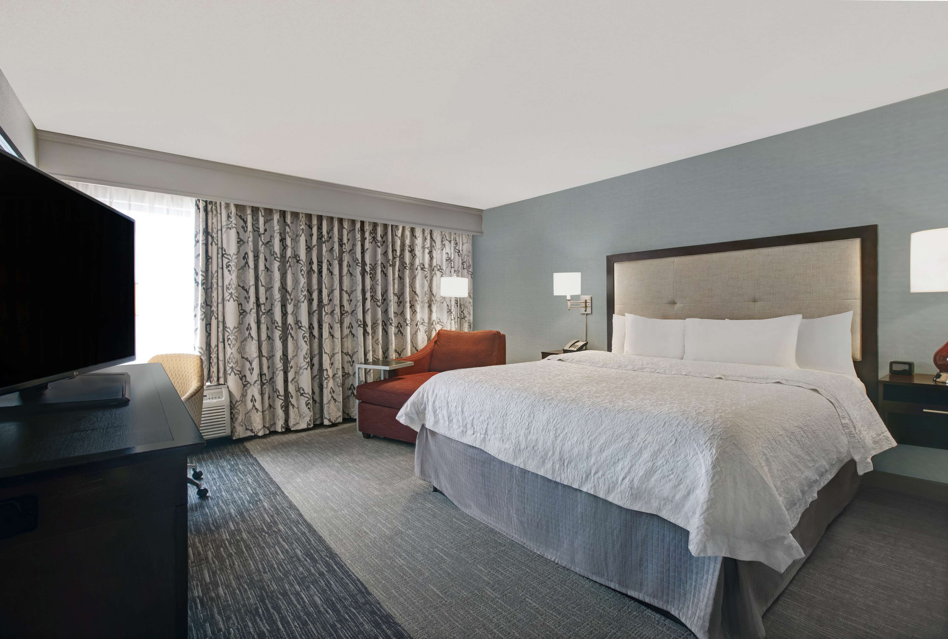 Quarto de hotel com cama grande, televisão, cadeira e escrivaninha.