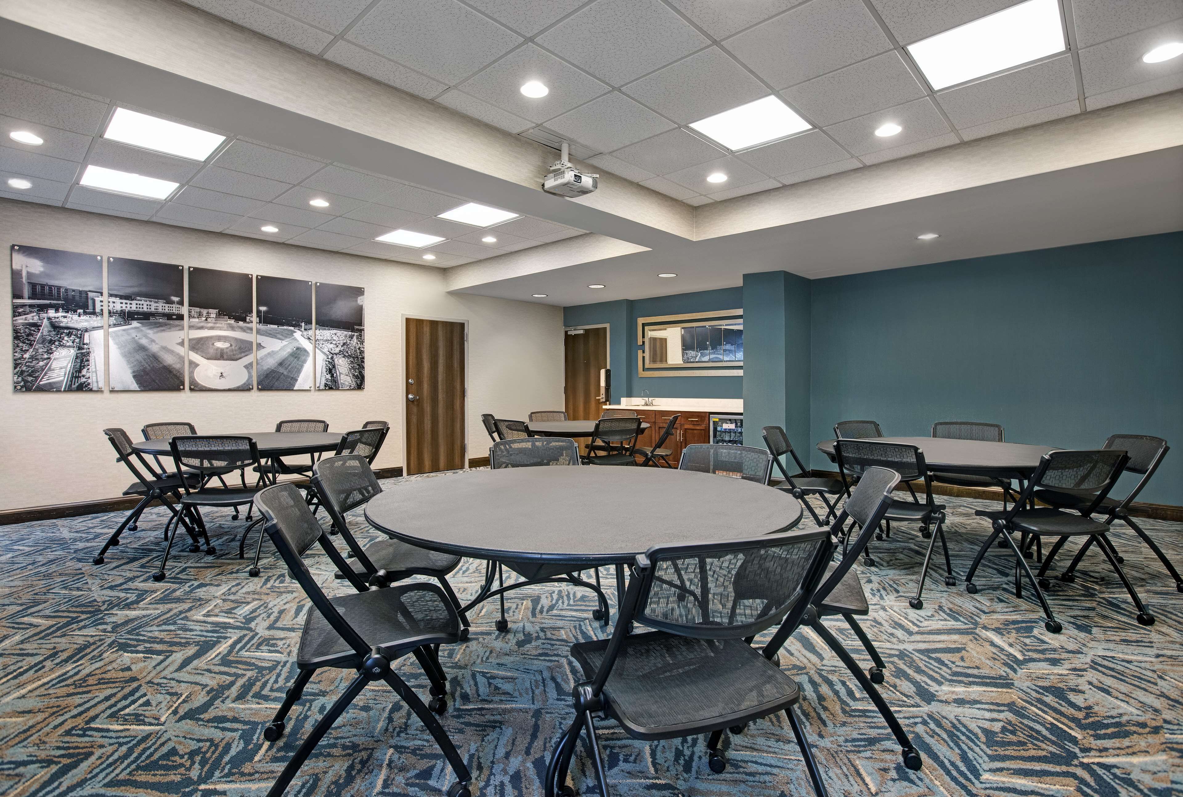 A conference room with a large round table, multiple chairs, a carpeted floor, and a ceiling with recessed lighting.