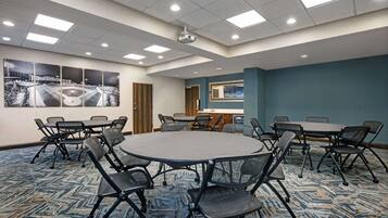 A conference room with a large round table, multiple chairs, a carpeted floor, and a ceiling with recessed lighting.