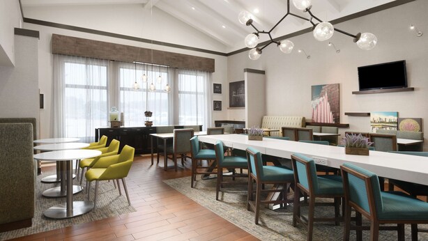 A modern dining area with a long table and chairs, a chandelier, and a television on the wall. - Hampton Inn & Suites Houston Medical Center NRG Park (Houston)