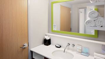 A hotel bathroom with a white sink, a mirror with a green frame, and a towel rack with neatly folded towels.