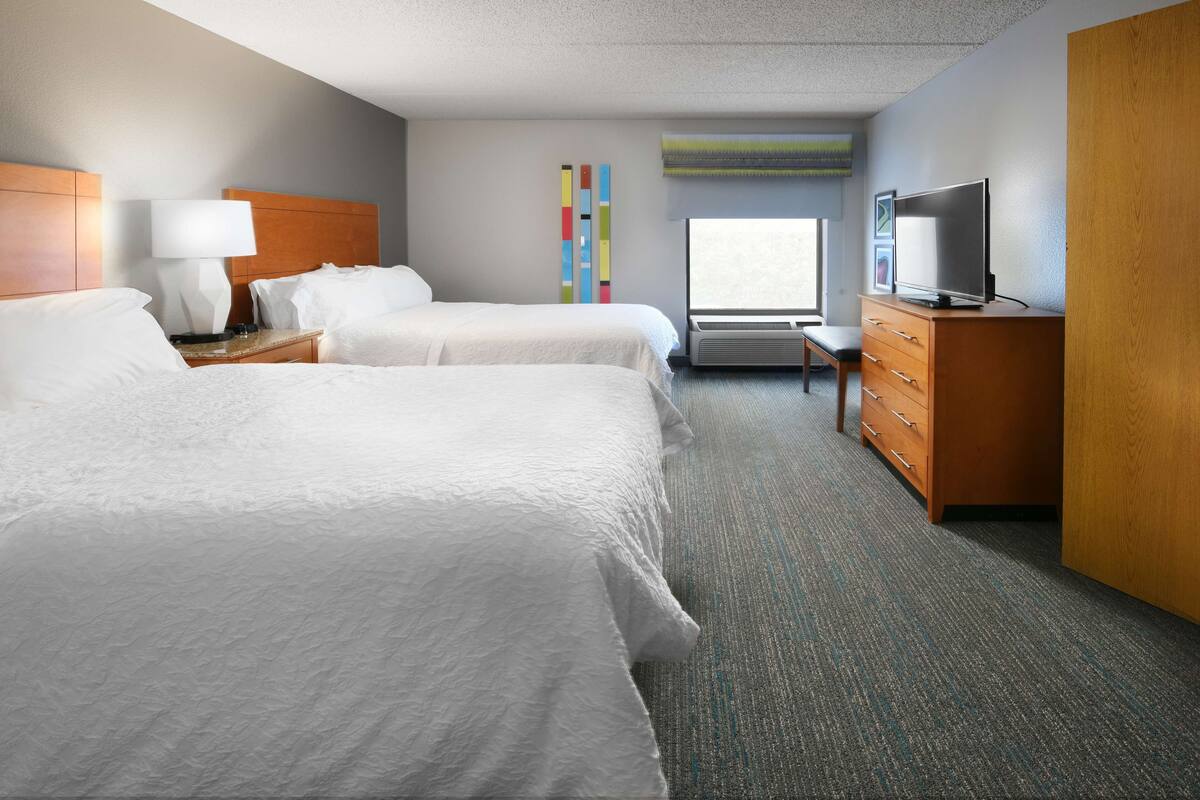 A hotel room with two beds, a TV, a dresser, and a window with a view.
