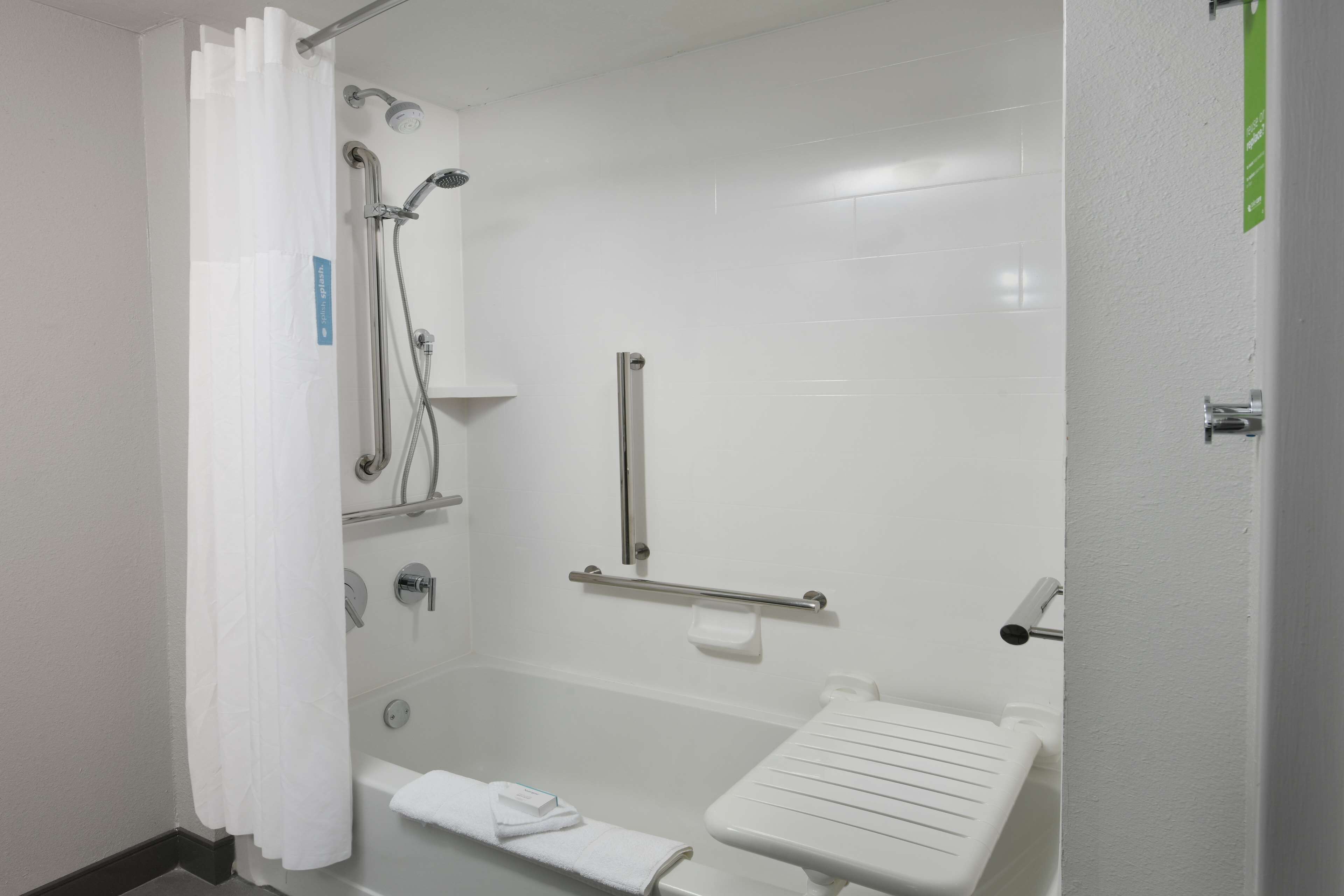 A modern bathroom with a shower, grab bars, a towel rack, and a toilet with a safety rail.