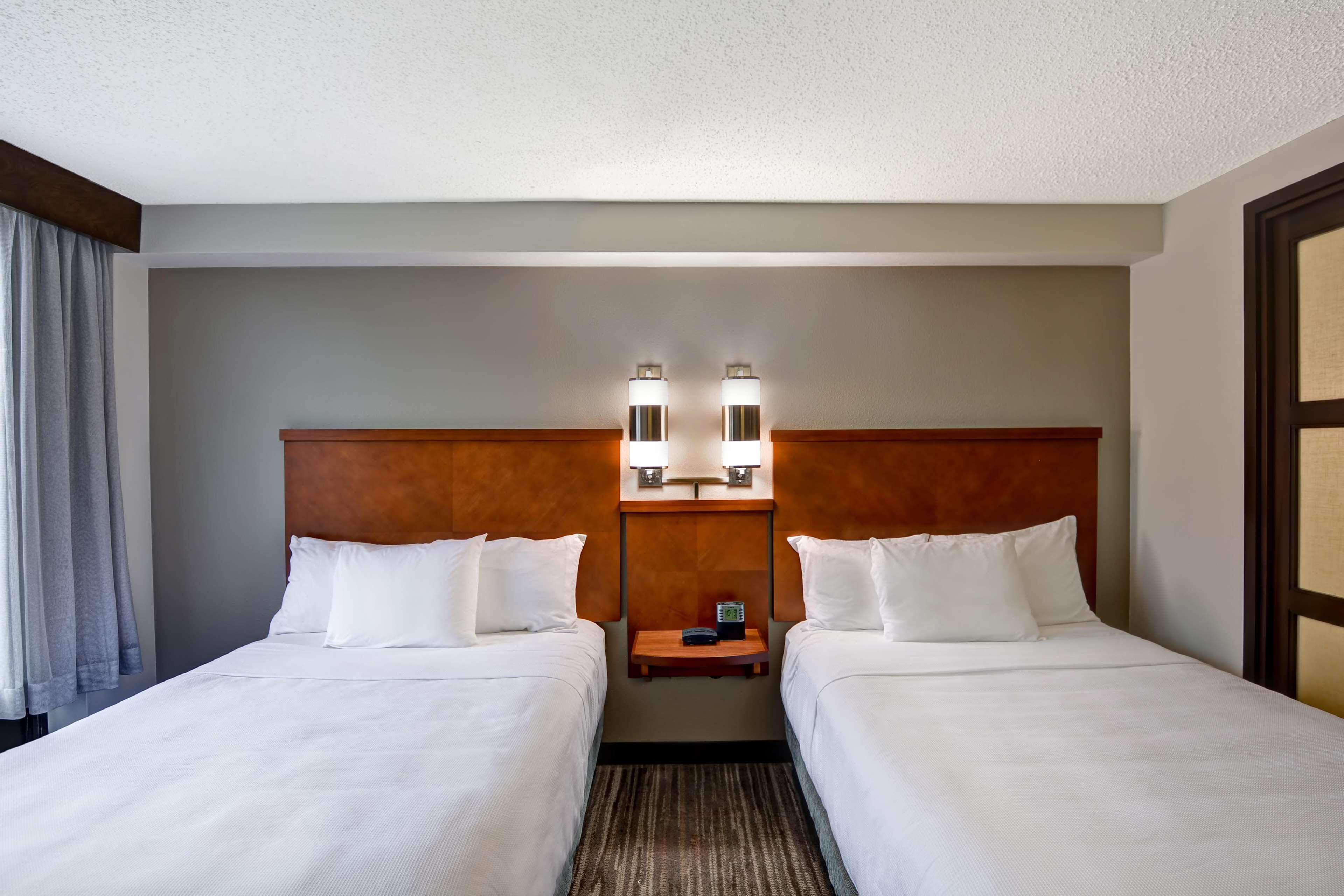 Une chambre d’hôtel avec deux lits, une tête de lit en bois, une table de chevet et deux lampes fixées au mur.