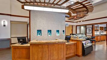 A hotel reception area with a curved wooden counter, a white brick wall, and a modern ceiling design.