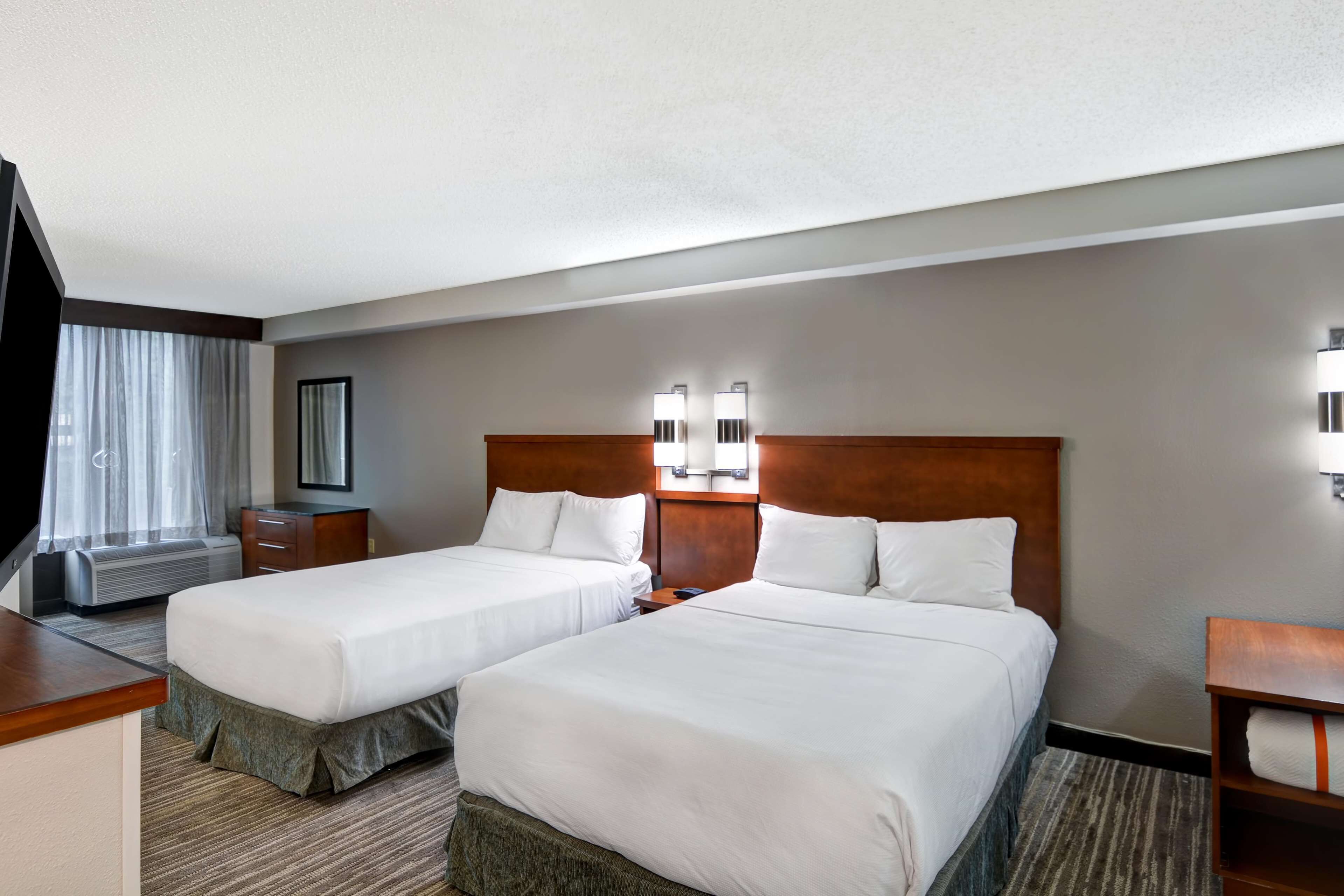 A hotel room with two beds, a desk, a chair, a TV, a mirror, and a window with curtains.