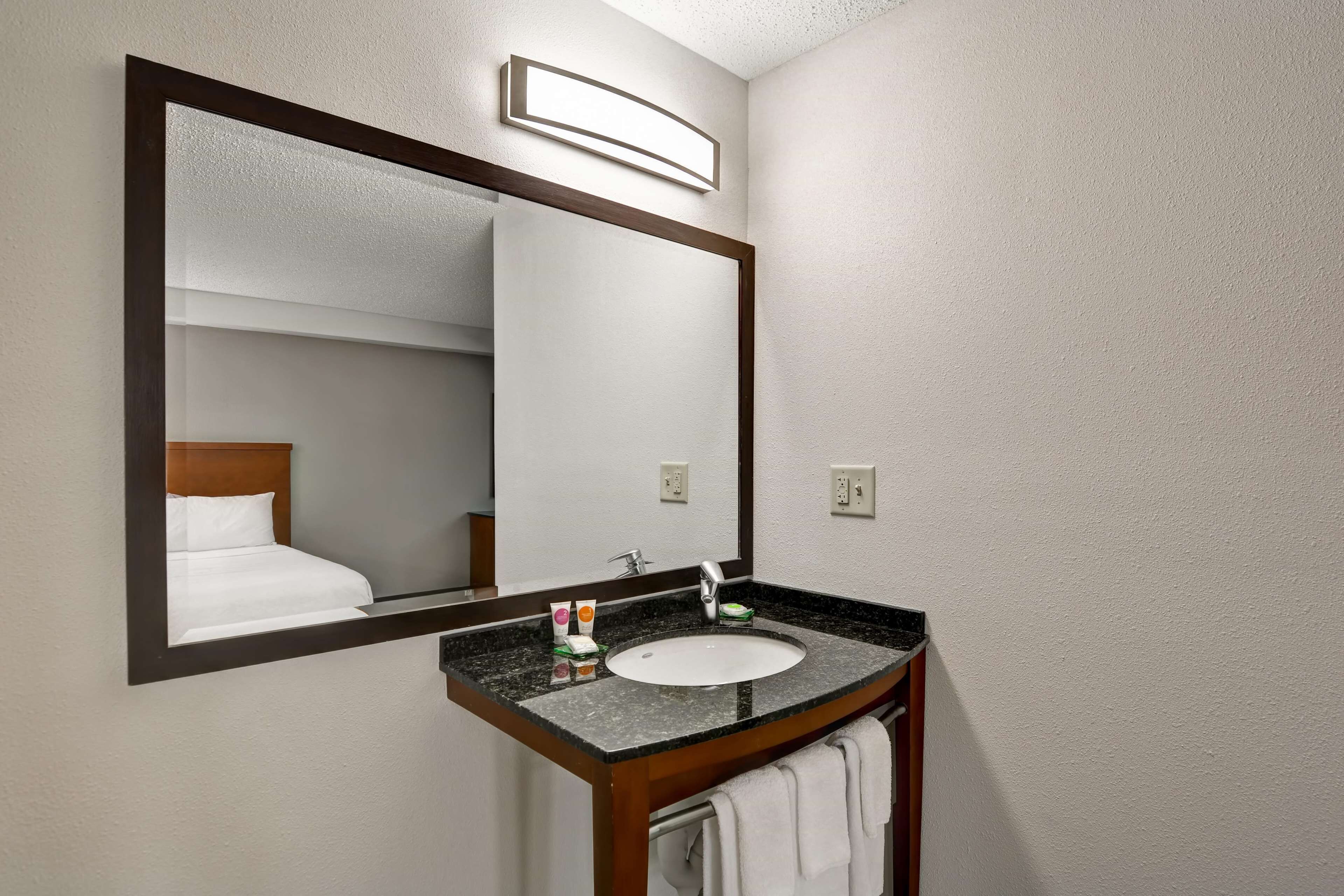 A bathroom with a large mirror, a sink, and a towel rack.
