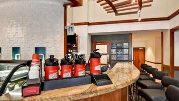 Zona de recepción de un hotel con un mostrador curvo de granito, una máquina de café Starbucks y exhibición de tazas con la marca Seattle's Best Coffee.