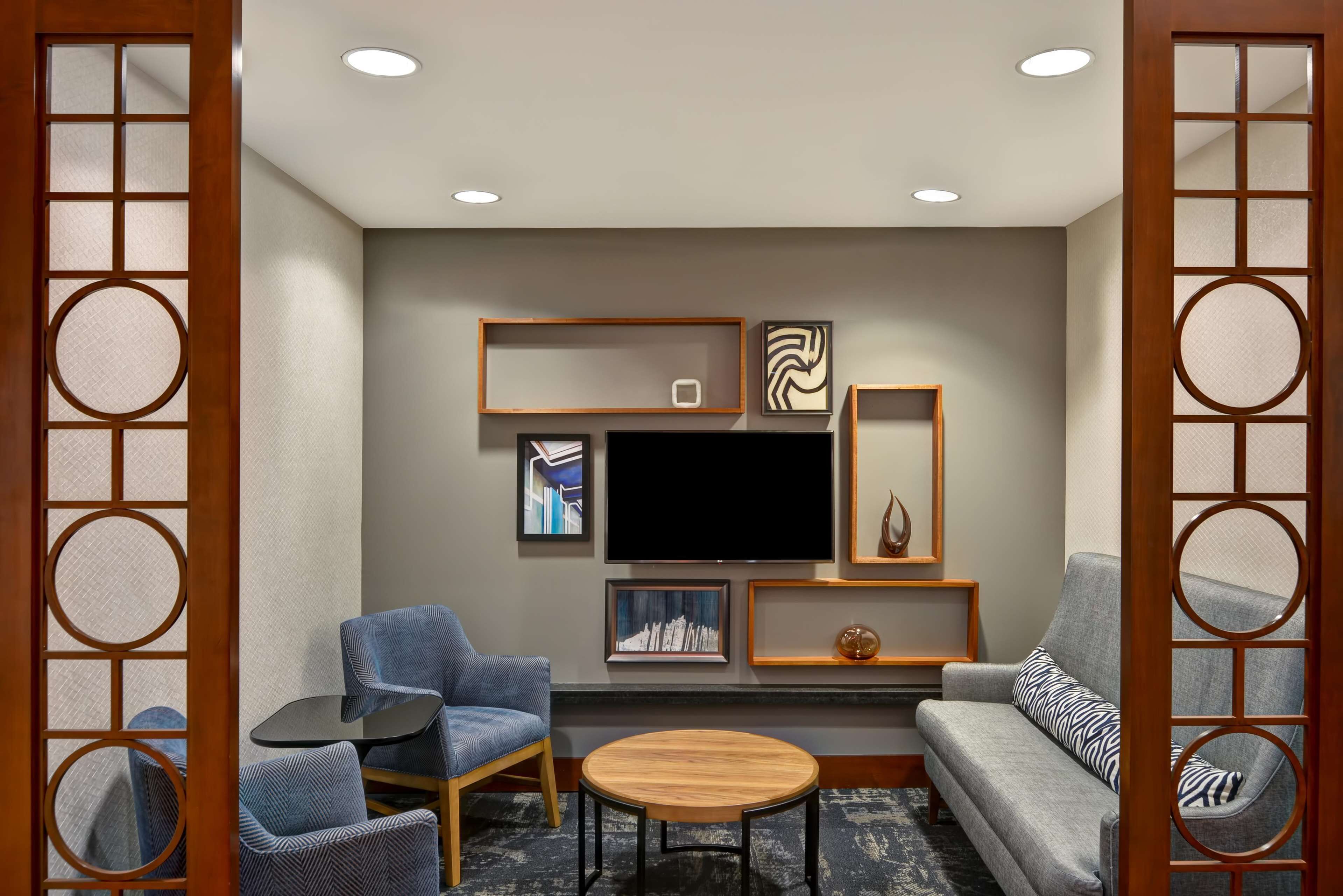 A modern living room with a grey sofa, two armchairs, a coffee table, and a flat-screen TV mounted on the wall.