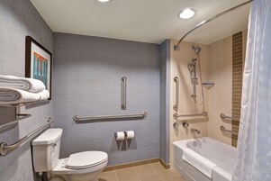 Un baño con inodoro, lavamanos, ducha con barras de apoyo y bañera.