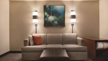 A neutral-toned living room with a gray sofa, a brown ottoman, and a painting on the wall.