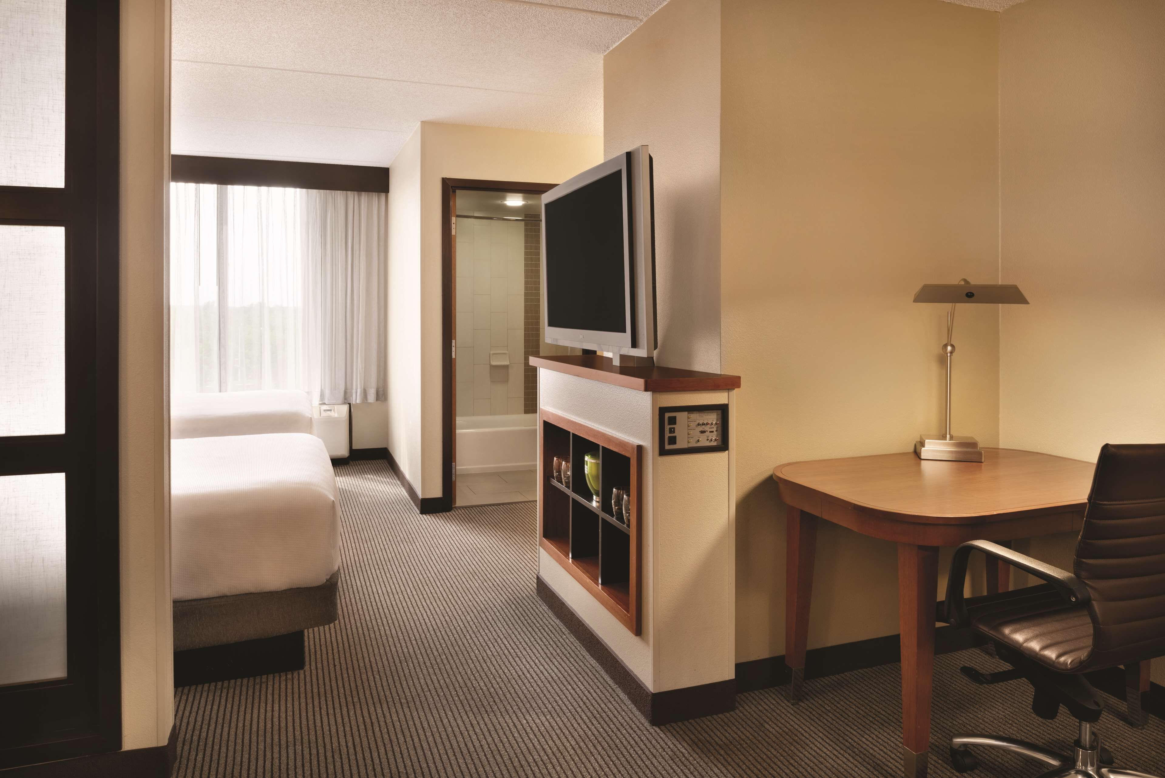 Habitación de hotel con cama, televisión, escritorio con silla y baño visible a través de una puerta abierta.