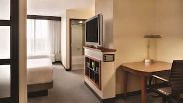 Habitación de hotel con cama, televisión, escritorio con silla y baño visible a través de una puerta abierta.
