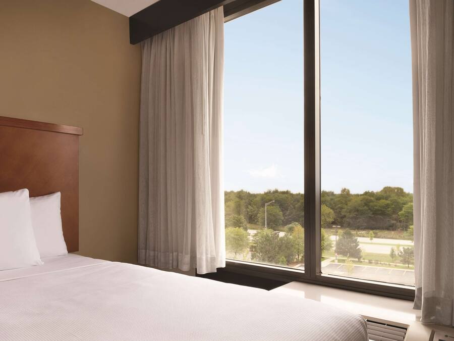A hotel room with a large window, a wooden headboard, and a neatly made bed.