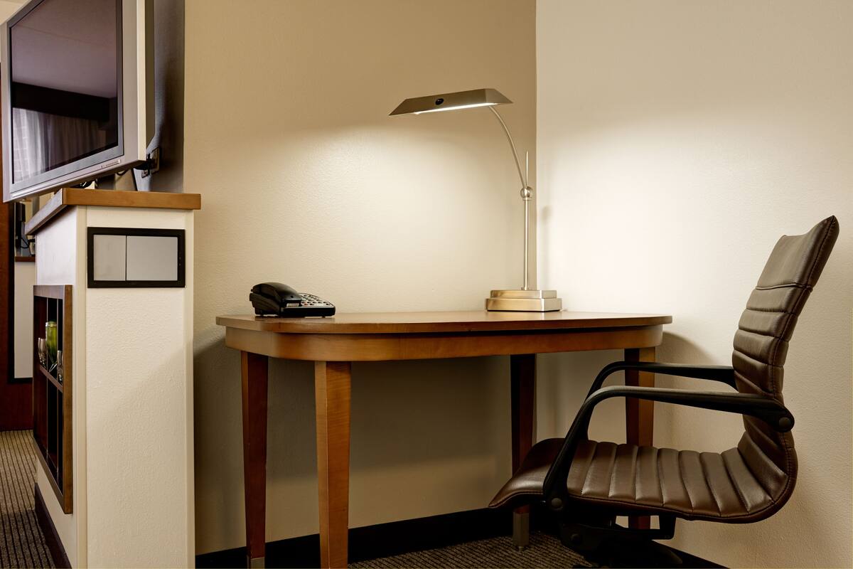 Habitación de hotel con un escritorio de madera, una silla, una lámpara de escritorio y un teléfono.