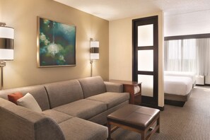 Ein Hotelzimmer mit Sofa, kleinem Tisch, einem Gemälde an der Wand, einer Lampe und einem Bett mit Blick aus dem Fenster.