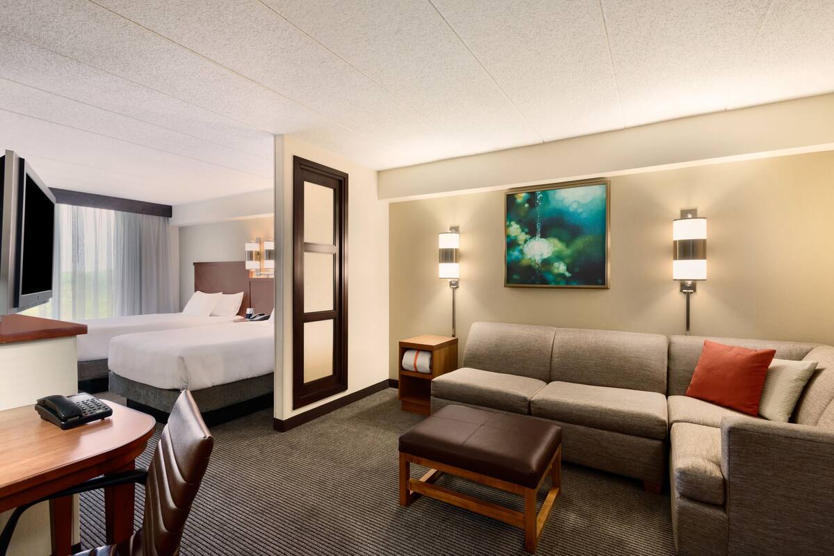 Habitación de hotel con cama, sofá, escritorio y teléfono, y dos lámparas de pared.