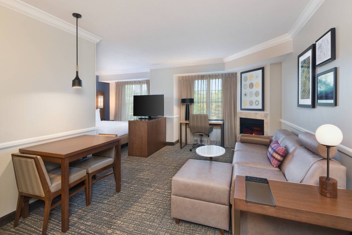 A hotel room with a dining area, a sofa, a TV, and a fireplace.