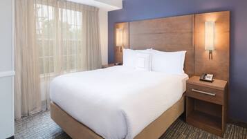 A hotel room with a large bed, two bedside tables with lamps, a telephone, and a window with sheer curtains.
