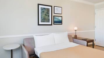 Habitación de hotel con una cama, una silla, una mesita redonda y dos cuadros en la pared.