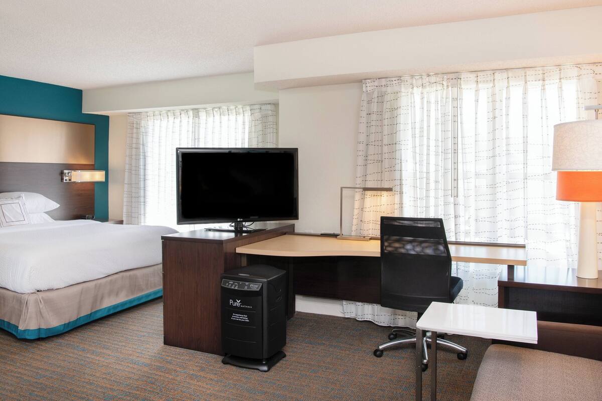 A hotel room with a bed, desk, chair, TV, and computer.