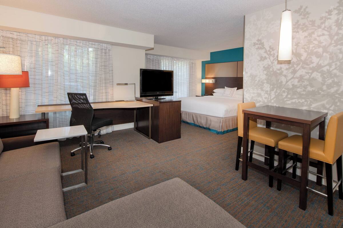 A hotel room with a bed, desk, chair, TV, and a small dining area.