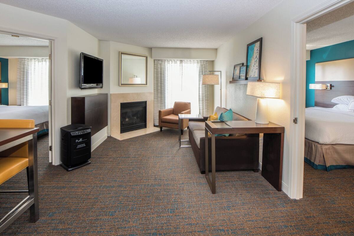 A hotel room with a bed, a desk, a chair, a television, a fireplace, and a carpeted floor.