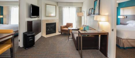 A hotel room with a bed, a desk, a chair, a television, a fireplace, and a carpeted floor.