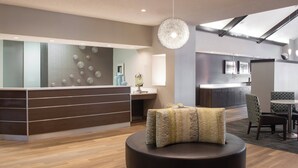 Eine moderne Lobby mit einer Rezeption, einer runden Sitzecke und einem Essbereich mit Tisch und Stühlen.