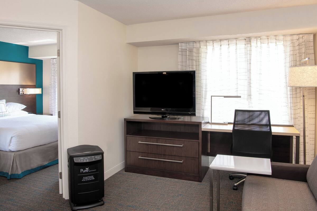 A hotel room with a bed, a desk with a computer, a TV, and a small cabinet.